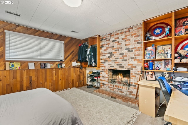 bedroom with wooden walls, a fireplace, and visible vents