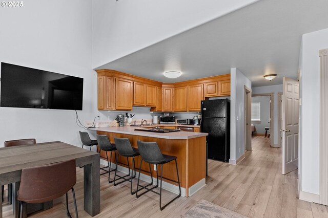 3979 NE Johns Ave, Neotsu, OR 97364 - kitchen featuring freestanding refrigerator, a peninsula, light wood finished floors, a sink, and a kitchen bar