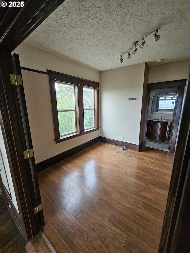 spare room featuring baseboards, a textured ceiling, wood finished floors, and track lighting