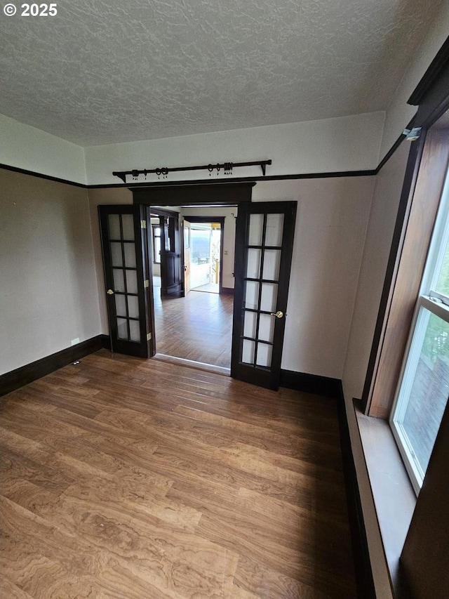 empty room with french doors, baseboards, a textured ceiling, and wood finished floors