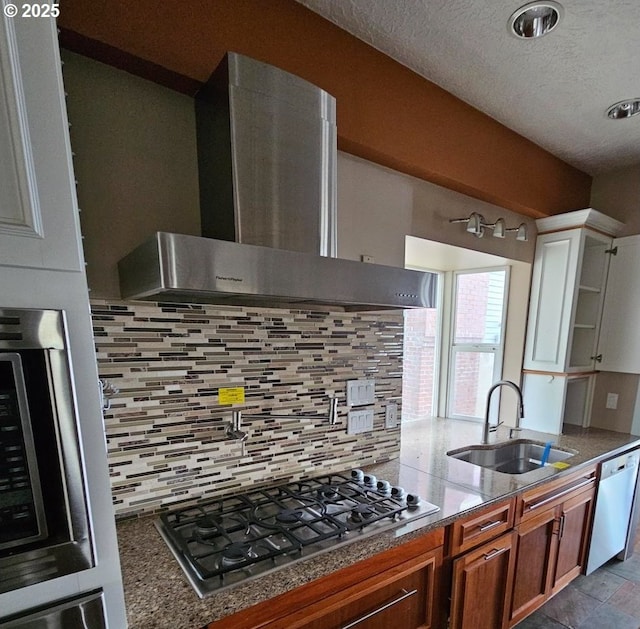 kitchen with dark stone countertops, wall chimney range hood, appliances with stainless steel finishes, and a sink