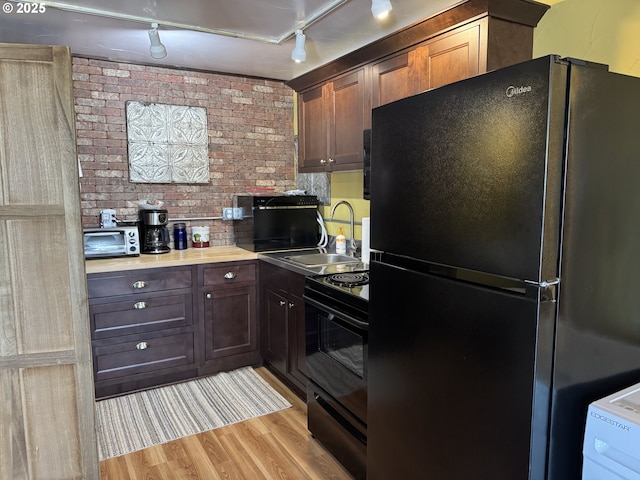 kitchen featuring dark brown cabinetry, sink, brick wall, light hardwood / wood-style floors, and black appliances