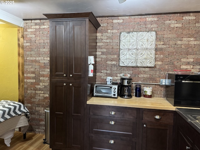 bar with dark brown cabinetry, brick wall, and light wood-type flooring