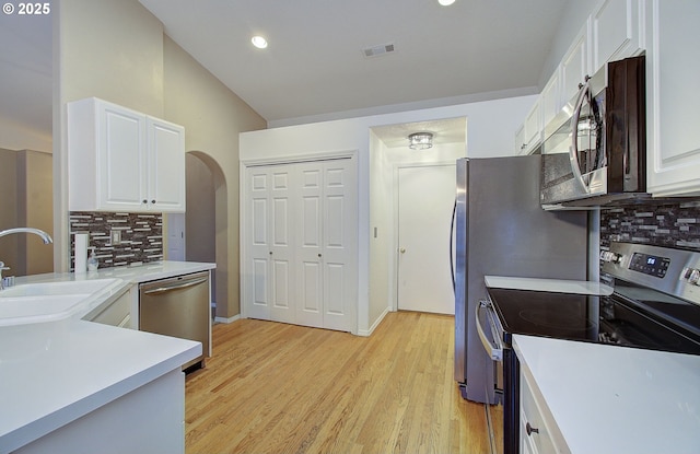 kitchen with tasteful backsplash, sink, white cabinets, light hardwood / wood-style floors, and stainless steel appliances