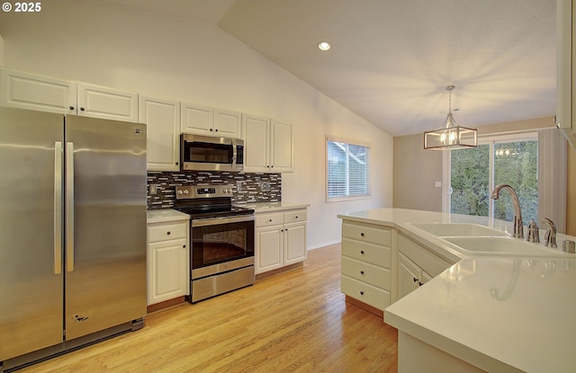 kitchen featuring stainless steel appliances, vaulted ceiling, sink, and decorative light fixtures