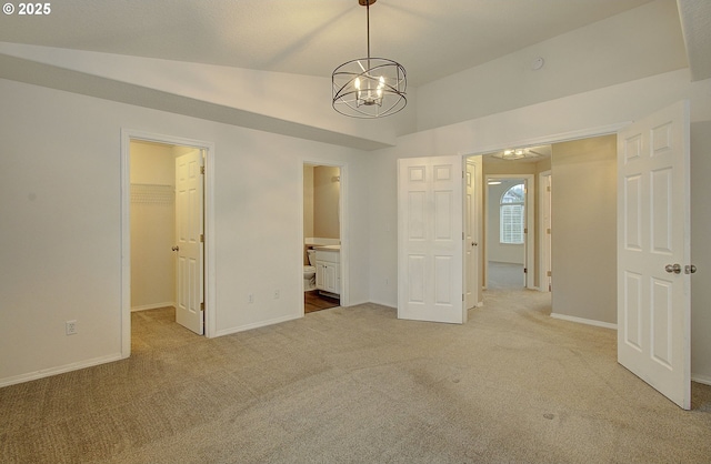 unfurnished bedroom featuring lofted ceiling, ensuite bathroom, carpet, a walk in closet, and a closet