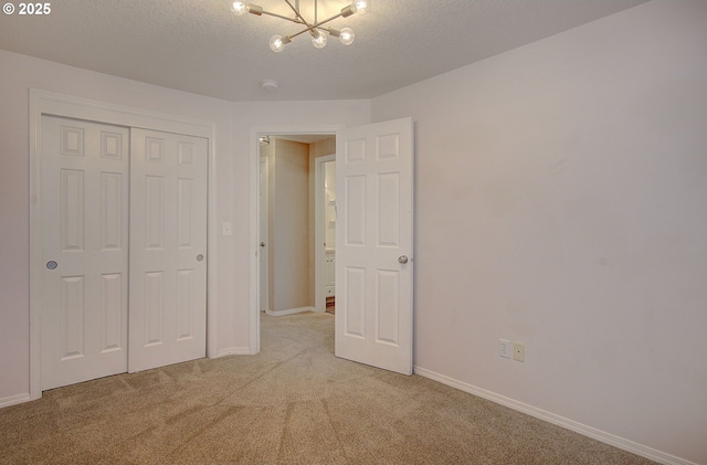 unfurnished bedroom with an inviting chandelier, a closet, light carpet, and a textured ceiling