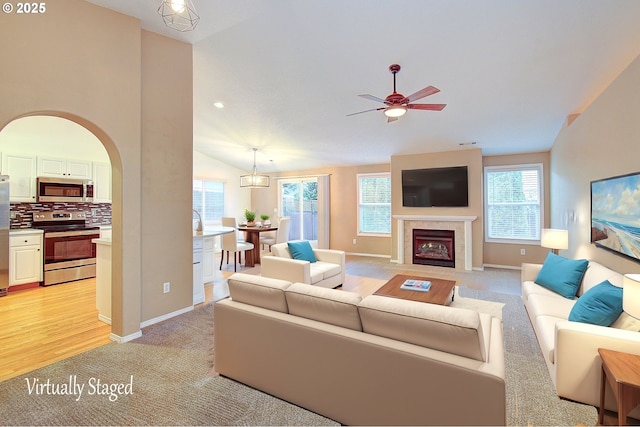 carpeted living room with ceiling fan, vaulted ceiling, and a tile fireplace