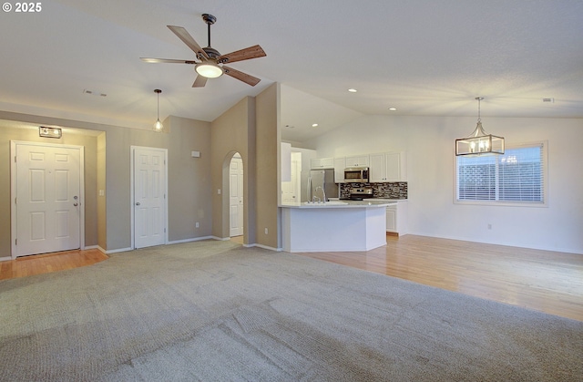 unfurnished living room featuring ceiling fan with notable chandelier, vaulted ceiling, and light carpet