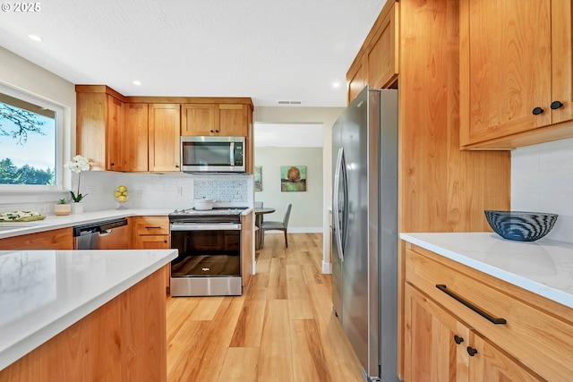 kitchen with tasteful backsplash, appliances with stainless steel finishes, and light hardwood / wood-style floors