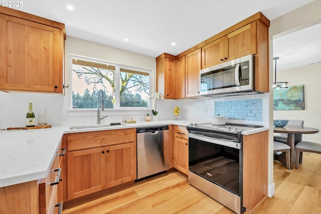 kitchen with tasteful backsplash, sink, light wood-type flooring, and appliances with stainless steel finishes