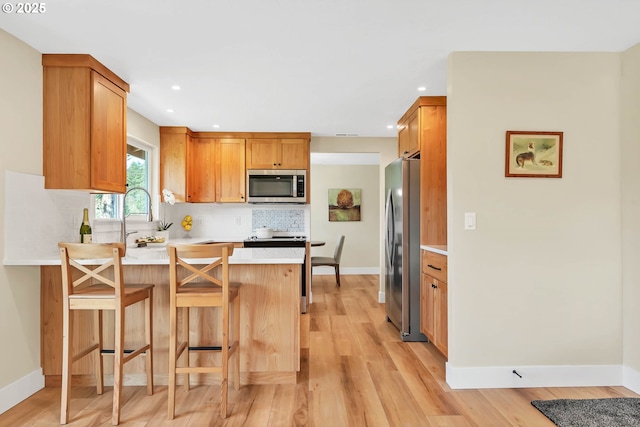 kitchen with a breakfast bar area, light wood-type flooring, appliances with stainless steel finishes, kitchen peninsula, and backsplash