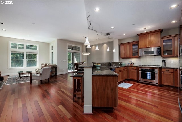 kitchen featuring a breakfast bar, a peninsula, open floor plan, brown cabinets, and appliances with stainless steel finishes