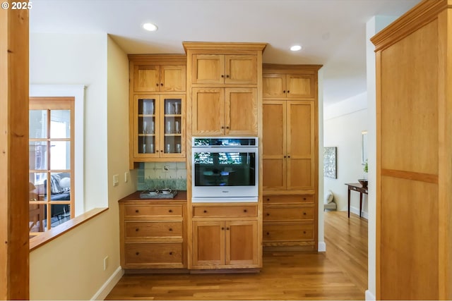 kitchen featuring oven, light wood-style flooring, backsplash, glass insert cabinets, and recessed lighting