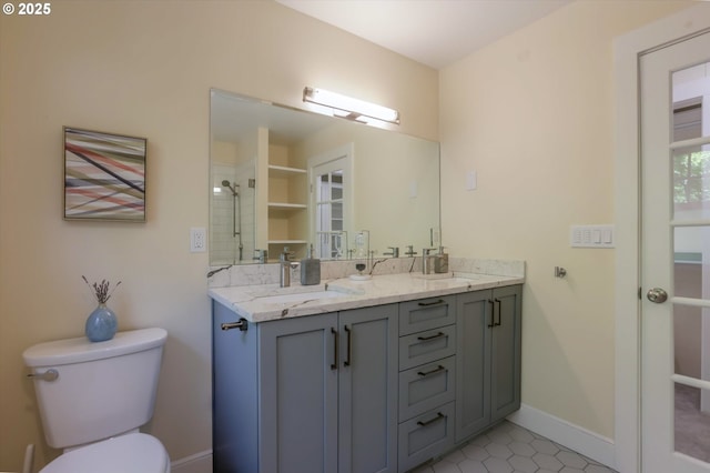 bathroom featuring toilet, double vanity, a shower, baseboards, and tile patterned floors