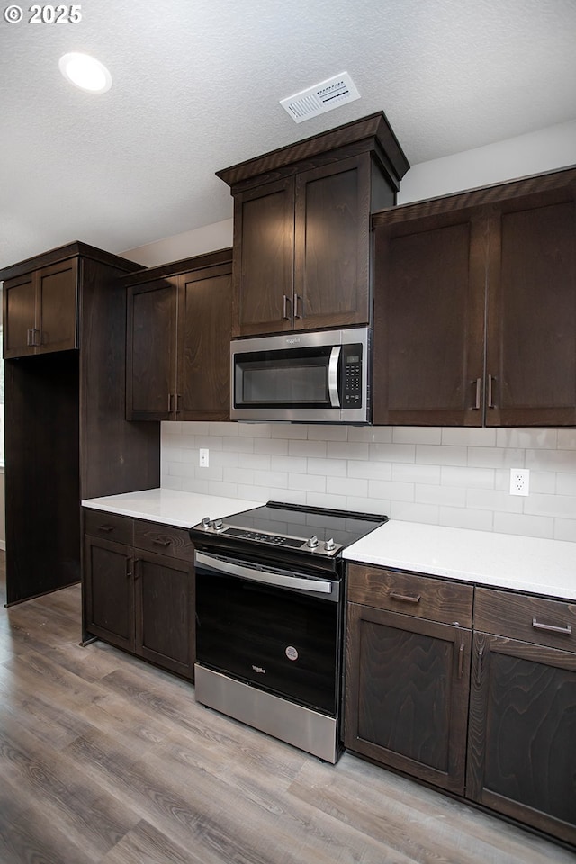 kitchen featuring dark brown cabinetry, a textured ceiling, light hardwood / wood-style flooring, stainless steel appliances, and decorative backsplash