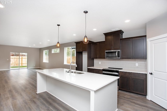 kitchen featuring sink, tasteful backsplash, dark brown cabinetry, an island with sink, and decorative light fixtures