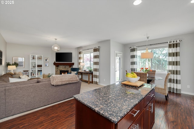 kitchen with open floor plan, dark wood-type flooring, hanging light fixtures, dark stone counters, and baseboards