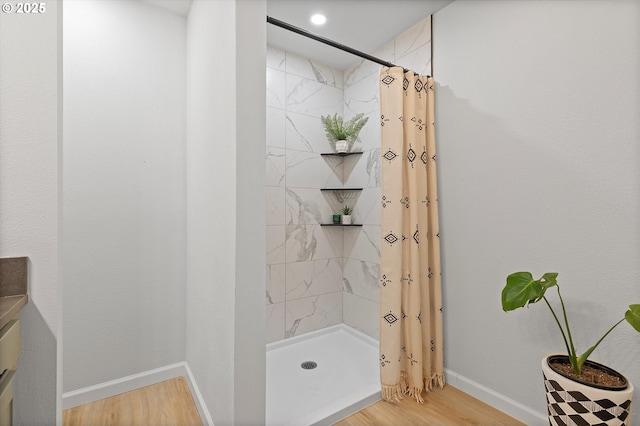 full bath with baseboards, a tile shower, and wood finished floors