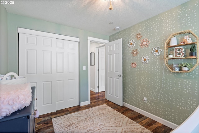 bedroom with baseboards, a textured ceiling, wallpapered walls, and wood finished floors
