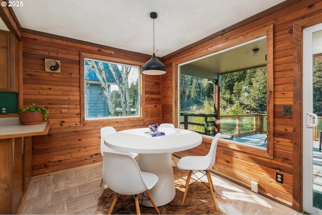 dining space with stone finish floor, wood walls, a wealth of natural light, and a textured ceiling