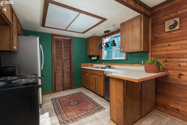 kitchen with a sink, black range with electric cooktop, a peninsula, brown cabinetry, and light countertops