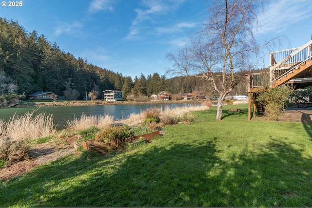 view of yard featuring stairs, a vegetable garden, a forest view, and a water view