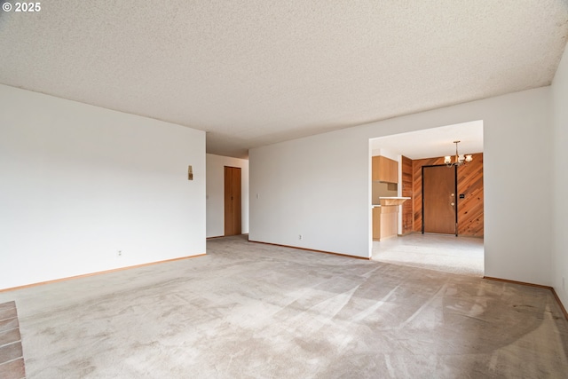 empty room featuring carpet, a notable chandelier, a textured ceiling, and baseboards