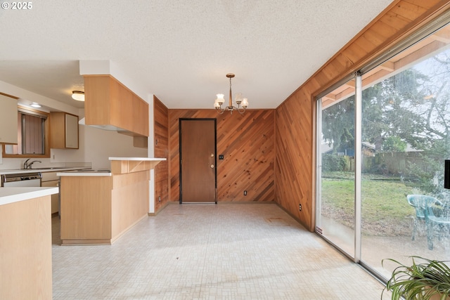 kitchen featuring pendant lighting, light countertops, an inviting chandelier, and wooden walls