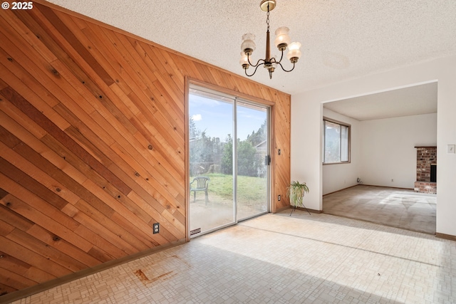 interior space featuring wood walls, a brick fireplace, a chandelier, and a textured ceiling