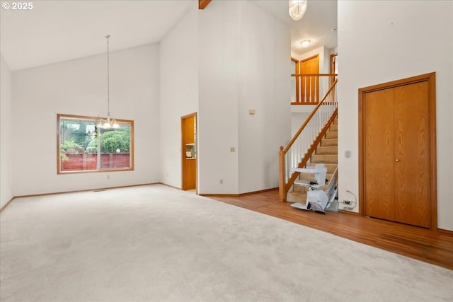 5002 SW Vacuna St, Portland, OR 97219 - unfurnished living room with high vaulted ceiling, carpet, a chandelier, stairway, and baseboards