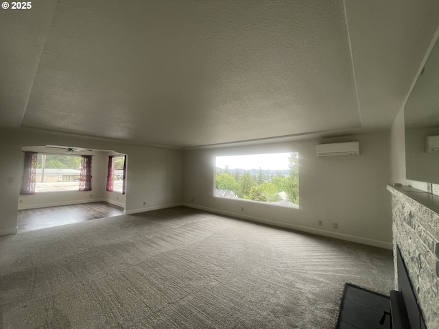 unfurnished living room featuring a wall mounted air conditioner, carpet, baseboards, plenty of natural light, and a textured ceiling