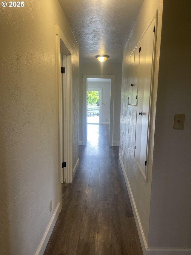 corridor featuring dark wood-style flooring, baseboards, a textured wall, and a textured ceiling