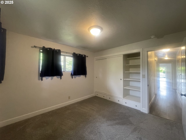 unfurnished bedroom with baseboards, dark colored carpet, a textured ceiling, and a closet