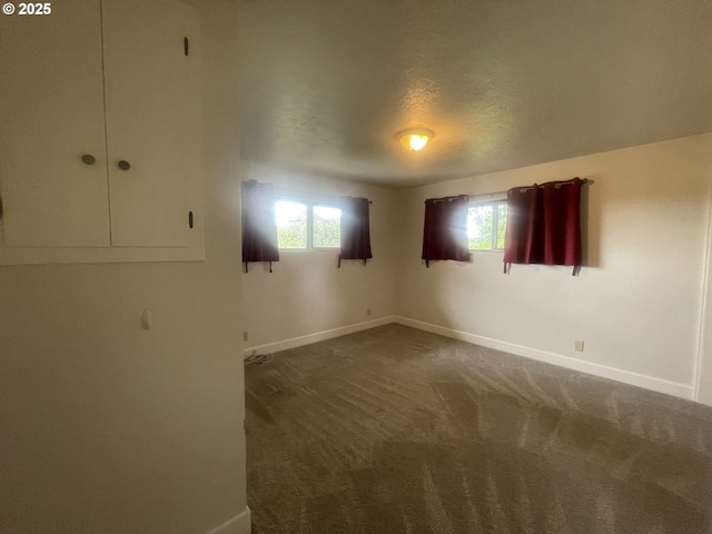 unfurnished bedroom featuring baseboards, dark carpet, and a textured ceiling