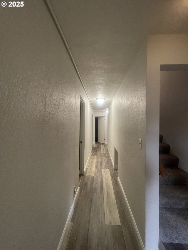 corridor featuring wood finished floors, a textured wall, stairs, and baseboards