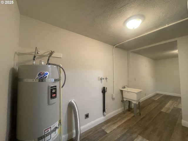 washroom featuring water heater, dark wood-type flooring, a textured ceiling, electric dryer hookup, and baseboards