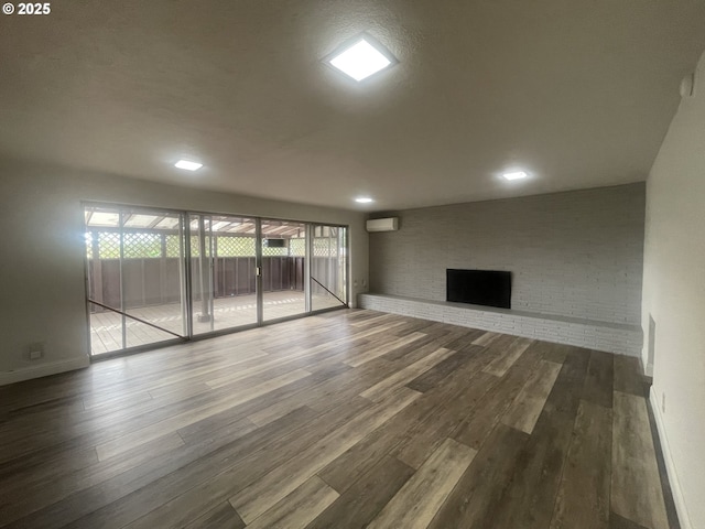 unfurnished living room with wood finished floors, a wall mounted AC, recessed lighting, brick wall, and a brick fireplace