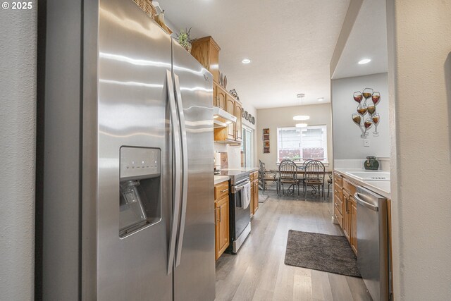 kitchen featuring stainless steel appliances, light hardwood / wood-style floors, and decorative light fixtures