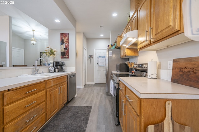 kitchen featuring pendant lighting, sink, appliances with stainless steel finishes, light hardwood / wood-style floors, and kitchen peninsula