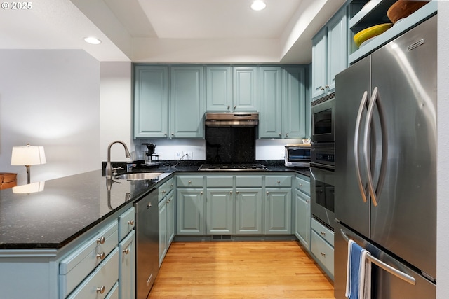 kitchen featuring appliances with stainless steel finishes, light wood-style floors, a sink, a peninsula, and under cabinet range hood