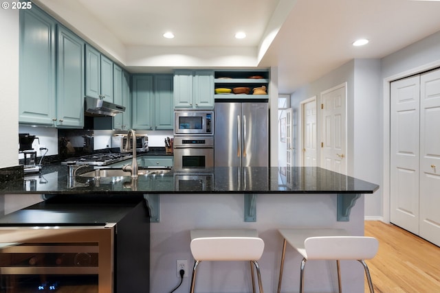 kitchen with under cabinet range hood, stainless steel appliances, a peninsula, blue cabinetry, and light wood finished floors