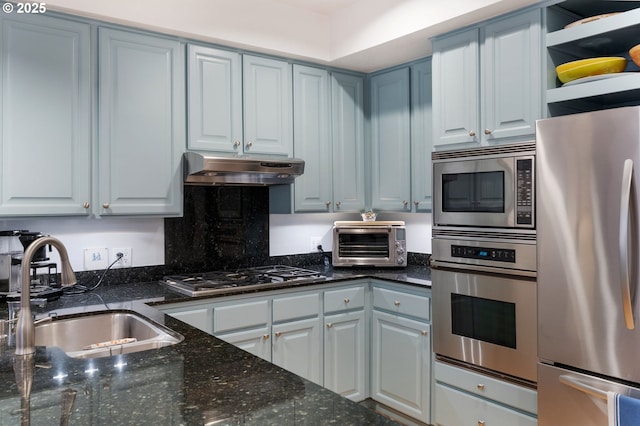 kitchen featuring a toaster, under cabinet range hood, a sink, appliances with stainless steel finishes, and dark stone countertops