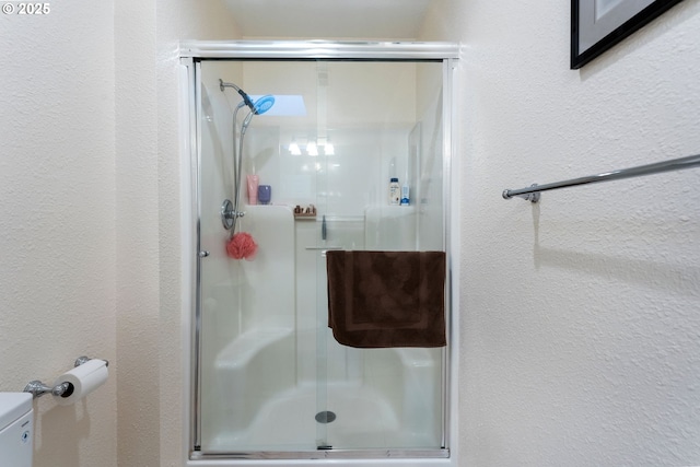 bathroom with a stall shower, a textured wall, and toilet