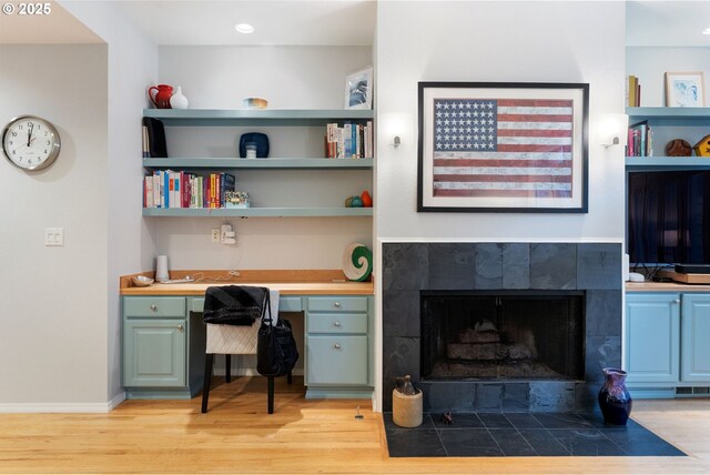 office area with baseboards, visible vents, a tiled fireplace, built in study area, and light wood-type flooring