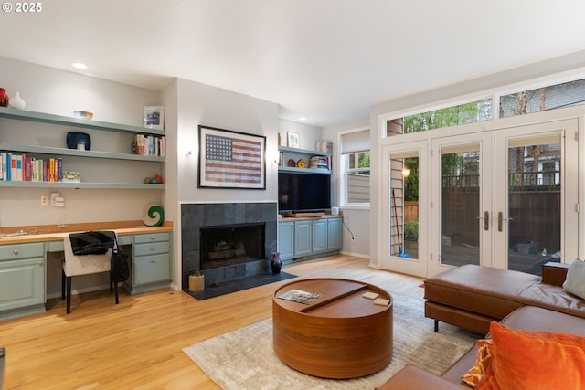 living room featuring a tile fireplace, recessed lighting, french doors, light wood-type flooring, and built in study area