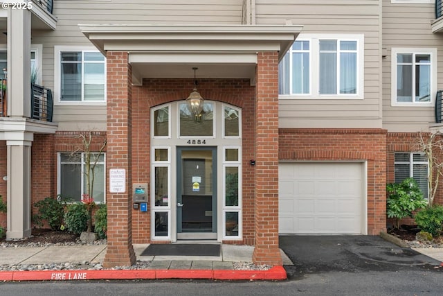 doorway to property featuring an attached garage, aphalt driveway, and brick siding