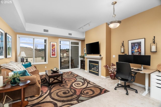 living room with baseboards, visible vents, a tiled fireplace, light colored carpet, and track lighting