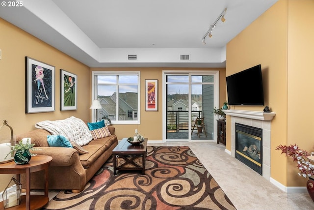 carpeted living room with baseboards, a tiled fireplace, visible vents, and track lighting