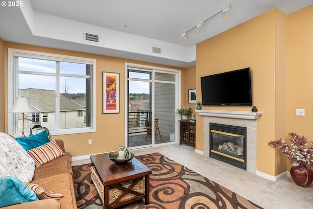 living area with a fireplace, visible vents, baseboards, carpet, and rail lighting